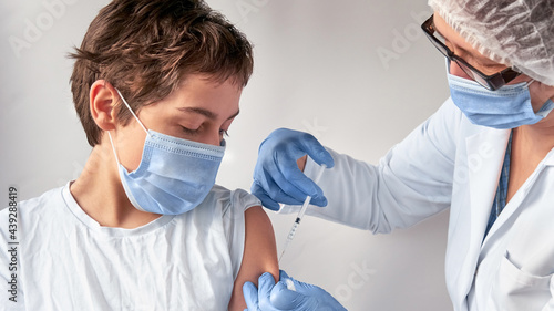 Vaccination of teenagers. Coronavirus, flu or measles vaccine concept. Medic, doctor or nurse with vaccine vial and syringe. Mature European female tech in protective white gown gives vaccine shot.