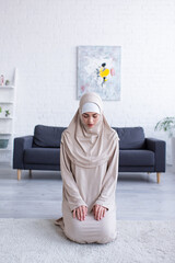 Wall Mural - young muslim woman praying while sitting on floor with closed eyes