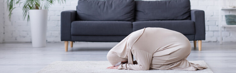 Wall Mural - arabian woman in hijab and abaya praying on floor at home, banner