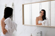 © New Africa - Happy young woman drying hair with towel after washing near mirror in bathroom