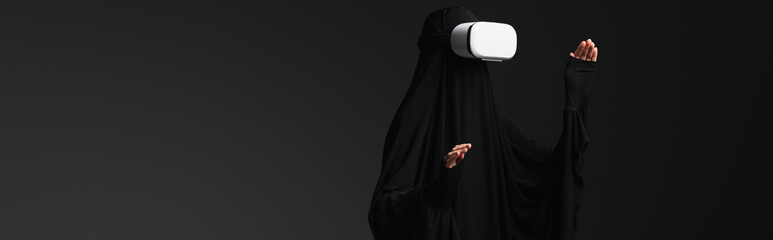 muslim nun gesturing while gaming in vr headset isolated on black, banner