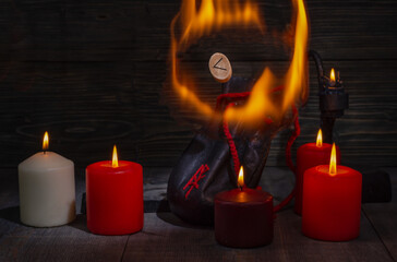 Wall Mural - Rune Kenaz surrounded by flames. A composition of burning candles, an old leather bag for Scandinavian runes with a bokeh effect.