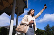 © Wavebreak Media - Caucasian businesswoman holding coffee cup and smartphone hailing a taxi on the street