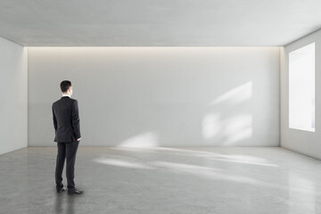 Wall Mural - pensive young businessman standing in white concrete interior with mock up place and windows with da