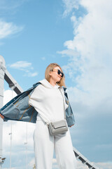 Wall Mural - Young woman urban lifestyle. Hipster in a white casual suit and jeans, spinning against the backdrop of the bridge and the blue sky. Summer walk