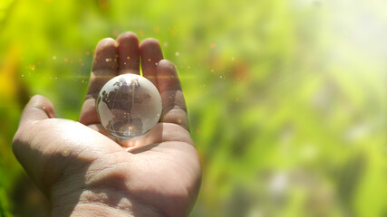 Card for World Earth Day or Arbor Day. Blue glass globe ball in human hand on blurred green background. Saving environment, save, protect clean planet and ecology, sustainable lifestyle.