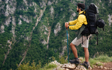 Wall Mural - Hiker young man with backpack and trekking poles looking at the mountains in outdoor