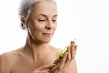 Wall Mural - Woman holding bottle with anti aging serum and looking at it while posing