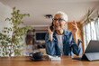 © bnenin - Senior woman, talking over the phone, at her home office.