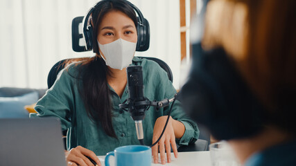 Wall Mural - Asia girl radio host record podcast use microphone wear headphone interview guest content wear mask protect virus conversation talk and listen in her room. Podcast from home, coronavirus quarantine.