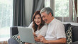 © tirachard - Asian senior couple using laptop at home. Asian Senior Chinese grandparents, surf the Internet to check social media while lying on sofa in living room at home concept.