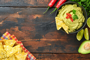 Guacamole. Traditional latinamerican Mexican dip sauce in a black bowl with avocado and ingredients and corn nachos. Avocado spread. Top view. Copyspace