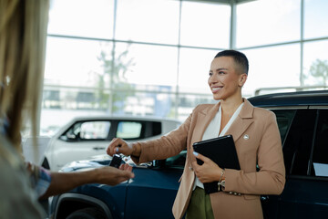 Wall Mural - Beautiful young saleswoman in car dealership giving keys to clients.