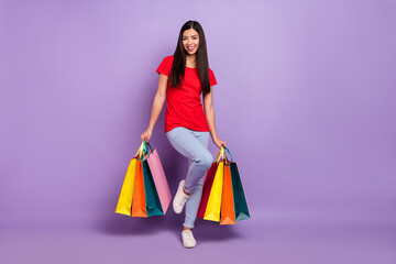 Full size photo of cool young brunette hairdo lady hold bags wear red t-shirt jeans isolated on violet color background