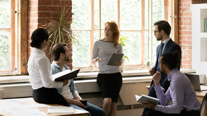 Poster - Professional female team leader holding digital computer tablet in hands, presenting business ideas to mixed race colleagues. Concentrated diverse coworkers discussing project development strategy.