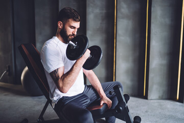 Determined caucasian male in active wear working on biceps muscles during workout in gym, serious strong sportsman keeping healthy lifestyle and perfect body shape using equipment for training