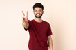 © luismolinero - Young Moroccan man isolated on beige background smiling and showing victory sign