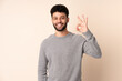 © luismolinero - Young Moroccan man isolated on beige background showing ok sign with fingers