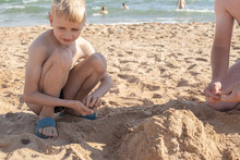 A Blond Boy On The Beach With His Father Are Building A Tower Out Of Sand. Summer Family Vacation On The Seashore