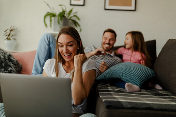 Wall Mural - Mother sits on the floor and celebrates the good news at work, while the father and daughter cuddle.