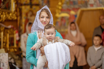 Wall Mural - The baptism of a baby in the temple, the mother holds the baby in her arms, a holy place, a church, reading prayers, a portrait of a baby close-up.
