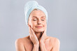 © denis_vermenko - Portrait of smiling senior woman feeling soft skin with hand after spa bath. Mature woman draped in towel looking at camera. Lady in bathrobe after shower isolated over white background.