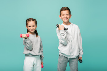 happy kids in sportswear working out with dumbbells isolated on blue.