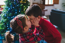 Kissing Siblings At Home With Christmas Tree