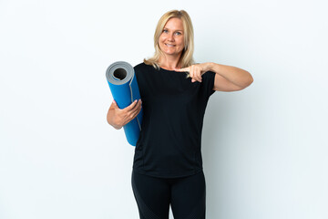 Wall Mural - Middle age woman going to yoga classes while holding a mat isolated on white background and pointing it