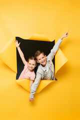 Wall Mural - happy children holding hands and smiling through hole on yellow background.