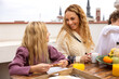© VICTOR TORRES/Stocksy - Smiling mother and daughter having breakfast on terrace