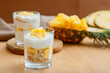 Tasty pineapple desserts with chopped fresh juicy pineapple. Breakfast dessert with oat granola, greek yogurt and pineapple in layers in glass with ingredients on wooden table