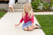 © Jennifer Bogle/Stocksy - Blonde girl sits on sidewalk with pink chalk