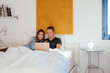 © David Prado/Stocksy - Optimistic couple using laptop on bed