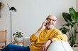 © BONNINSTUDIO/Stocksy - Happy aged male speaking on smartphone on couch