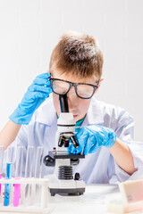 Wall Mural - a schoolboy with a microscope examines chemicals in test tubes, conducts experiments - a portrait on