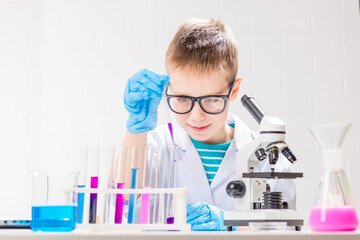 Wall Mural - a schoolboy with a microscope examines chemicals in test tubes, conducts experiments - a portrait on