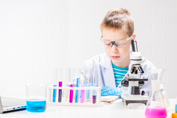 Wall Mural - a schoolboy with a microscope examines chemicals in test tubes, conducts experiments - a portrait on