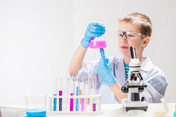 Wall Mural - a schoolboy with a microscope examines chemicals in test tubes, conducts experiments - a portrait on