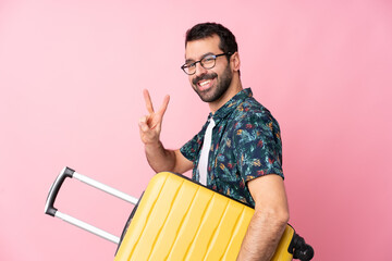 Young caucasian man over isolated background in vacation with travel suitcase and making victory gesture