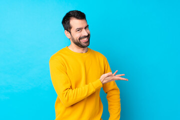 Sticker - Young caucasian man over isolated blue background presenting an idea while looking smiling towards