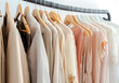 Stylish womans clothes hanging on a rack natural colors, trending concept,pastel colors in white room modern design closeup