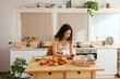 © BONNINSTUDIO/Stocksy - Young woman using smartphone near fruits in kitchen