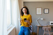 © BONNINSTUDIO/Stocksy - Happy young woman using smartphone near window