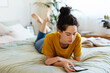 © BONNINSTUDIO/Stocksy - Young woman reading e book on bed