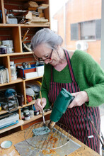 Senior Grey-haired Woman Applies Patina To A Small Bronze Sculpture Smiling