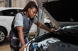 © Roman - Tired african auto mechanic woman misunderstanding what is wrong with car, looking inside of hood, side view portrait. Young female in auto service. copy space