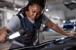 © Roman - african woman mechanic looking to car engine and holding lamp, Car master in service shop, female mechanic repairer service technician checks and repairs the engine condition under hood of vehicle
