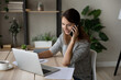 © fizkes - Smiling woman talking on smartphone, looking at laptop screen, confident businesswoman working online, consulting client by phone call or negotiating, discussing project with colleague, multitasking