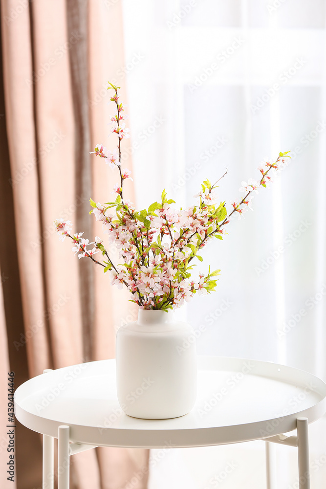 Vase with beautiful blooming branches on table in room